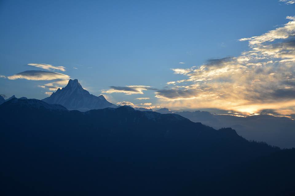 Sharp snow-covered Himalayan peak at sunrise with golden sky and dark ridges in foreground.