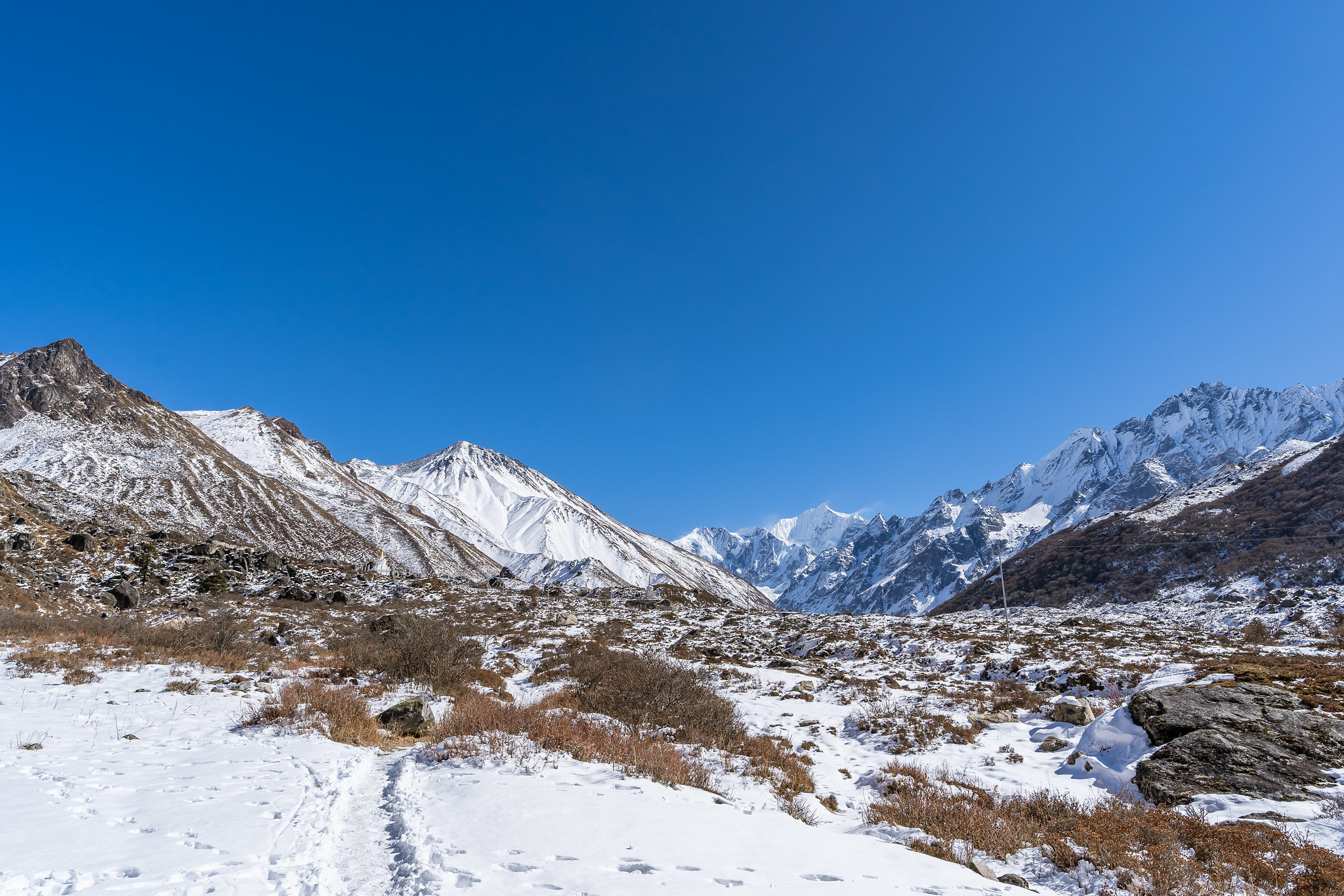 Snow-covered mountain path leading to jagged Himalayan peaks under a clear blue sky.