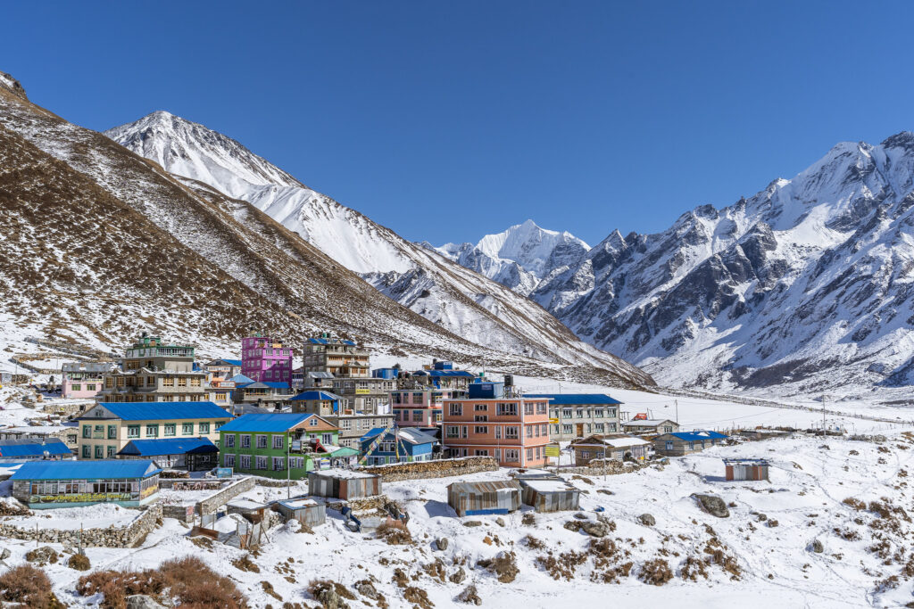 Colorful Himalayan mountain village with blue-roofed houses nestled in snowy valley beneath rugged peaks.