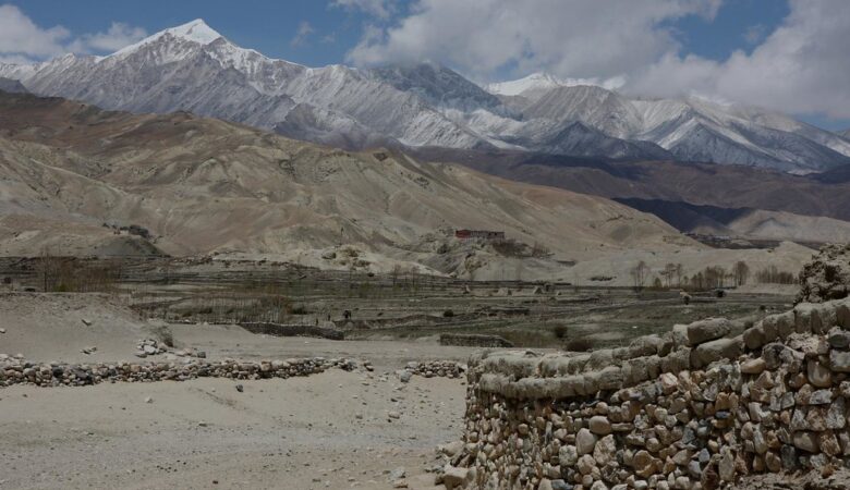 "Snow-capped Mustang Himalayas with terraced fields and stone wall."