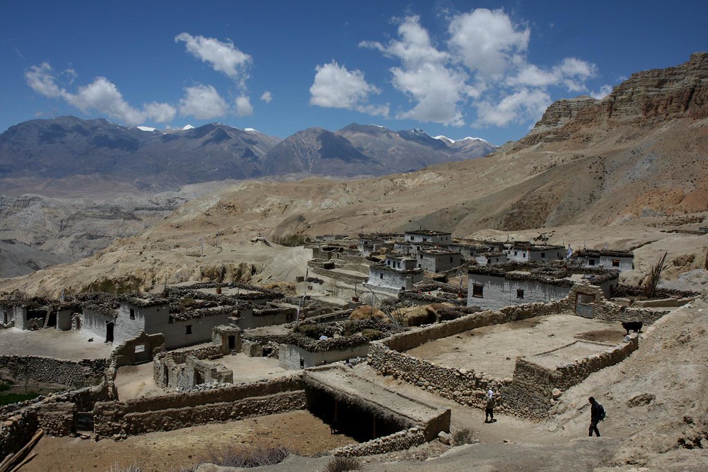 Remote Himalayan mountain village with stone houses, terraced ground, and snowy peaks in the background.