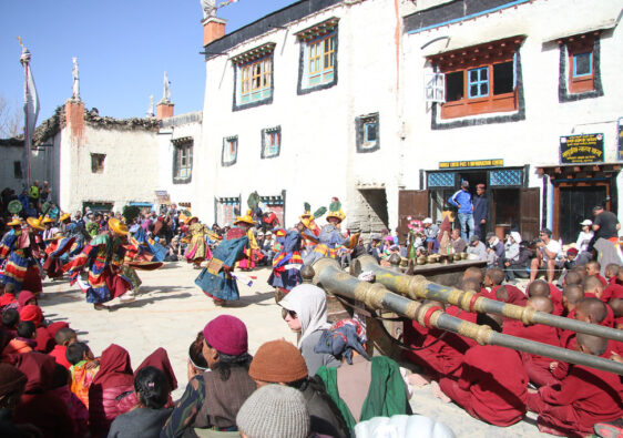 "Colorful Mustang festival with dancers in yellow hats, Tibetan-style courtyard, monks, and ceremonial horns."