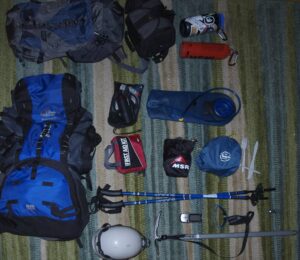 Carefully arranged mountaineering gear on a rug, including backpack, duffel bags, water bottles, first aid kit, trekking poles, helmet, and ice axe, ready for an expedition.