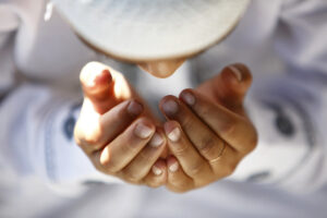 Hands cupped in prayer wearing white garment and cap.