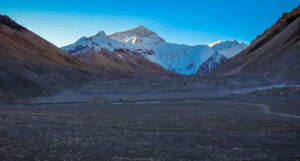 Mount Everest viewed from the Tibetan side, rising above a barren rocky plain with a winding dirt path.