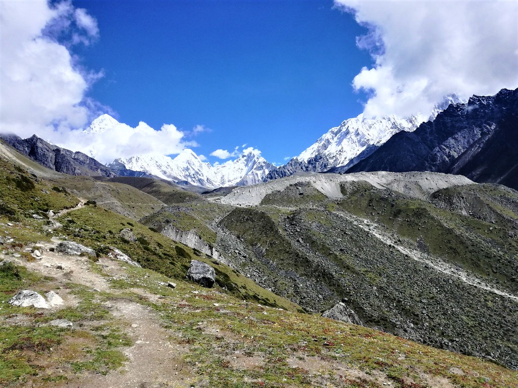 Mountain trail leading toward towering snow-covered Himalayan peaks under a bright blue sky
