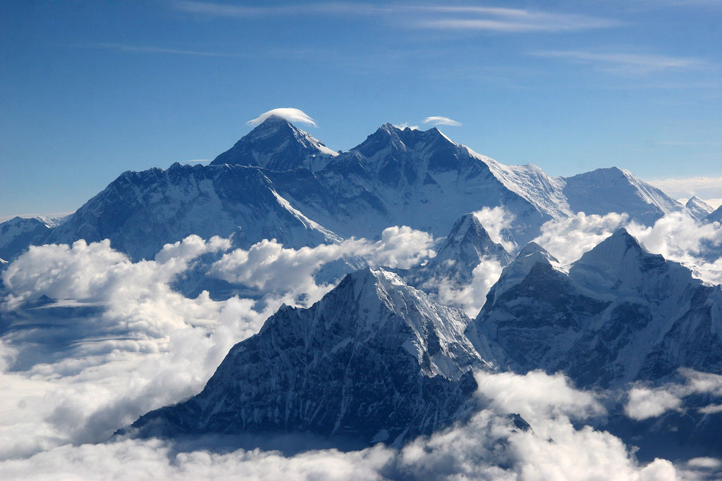 Mount Everest with a lenticular cloud above its peak, surrounded by snow-covered Himalayan mountains and drifting mist.