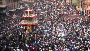 Crowd gathered in historic square around ornate wooden chariot with pagoda-style roof during festival procession.