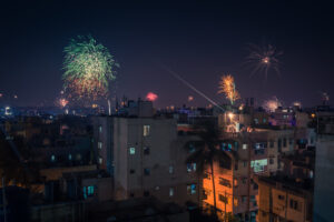 Colorful fireworks exploding above illuminated city buildings during a nighttime festival celebration.