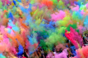 Crowd throwing colorful powder into the air during Holi festival celebration, creating vibrant clouds of color.