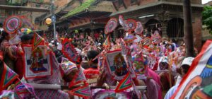 Crowd with colorful flags and paper decorations during street festival in front of brick buildings.