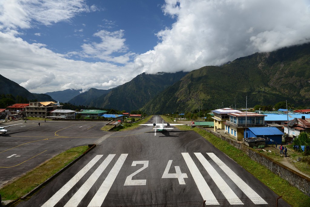 “Small Himalayan airport runway with aircraft and colorful village roofs”