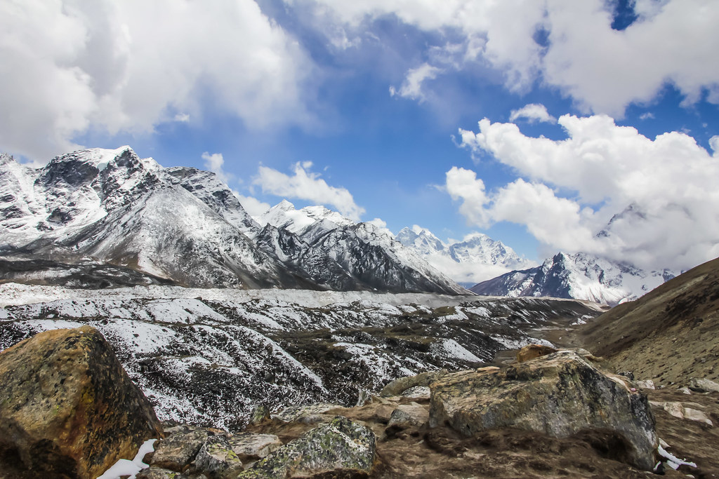 "Rugged Himalayan mountains with snow-covered peaks under blue sky and clouds"