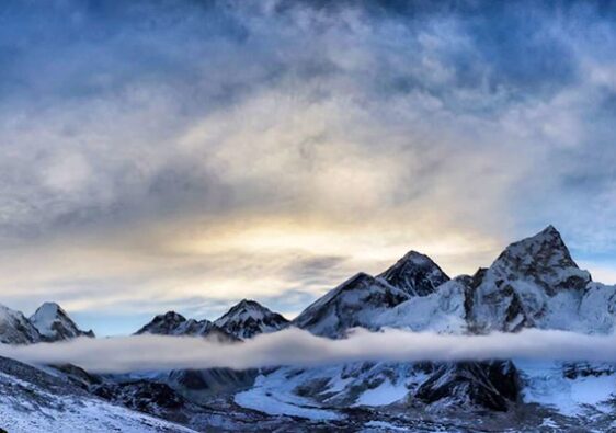 "Panoramic view of snowy Himalayan peaks with mist and sunlight over rugged summits"